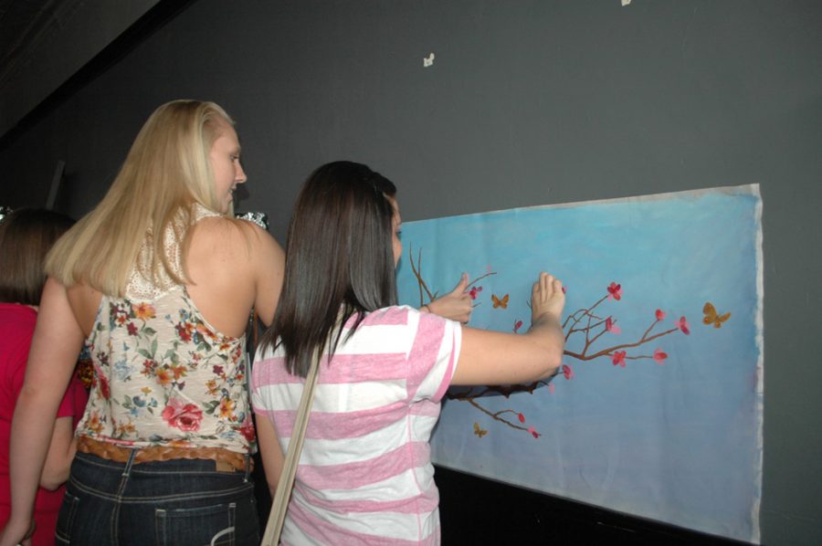 Seaman grads and former basketball team members Kara Lee and Kylie Shugart leave their fingerprints on a painting designed by art teacher Stephanie Munoz-ONeil.  Earlier in the day, current members of the basketball left their prints on the painting in memory of their coach.