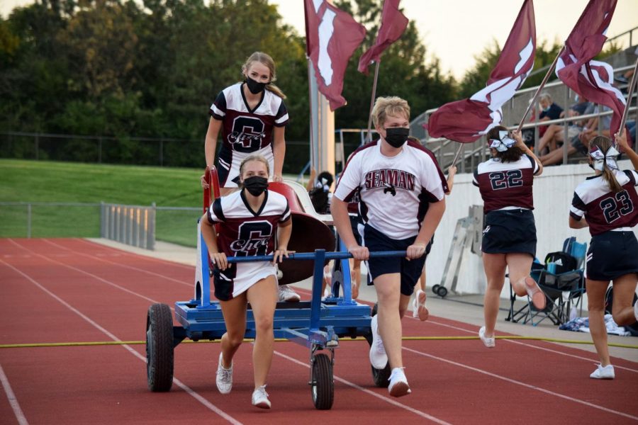 Seniors and Hannah Watkins, Isabel Freisberg Tyler Parkhurst run the bell at the scrimmage on August 28.  The cheerleaders wore their masks and practiced social distancing throughout the game.