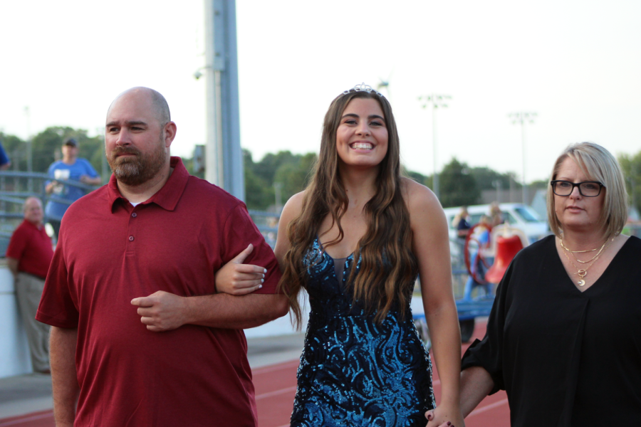 Homecoming candidate Drew Baxter happily smiles to the camera while her mother and father walk her down the track during the Homecoming crowning. 