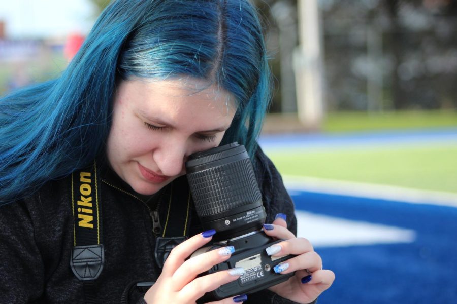 Junior yearbook staffer, Jocelynn Ginn, curiously looks into her camera while taking photos at the Apr. 25, 2022, girls soccer game against Shawnee Heights.